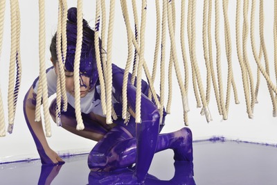 A close-up of the figure on all fours. Upper body touching the rope.