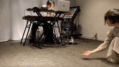 A pose extending one hand toward, Risa as she operates upper and lower buttons