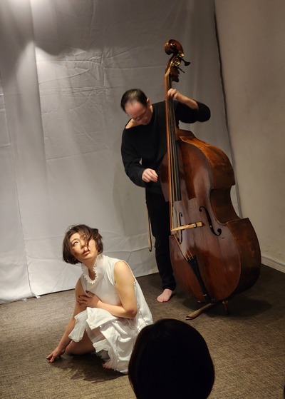 Crouching and looking upward; the contrabass stands behind