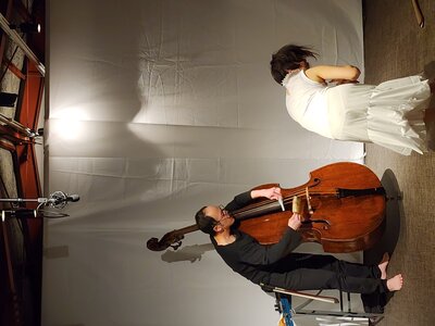 Tajima switches the bow to a smaller instrument and plucks; upper body bent in a half-squat