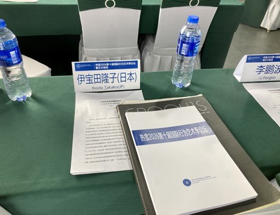 On the forum tables: green tablecloth, nameplate, documents, water