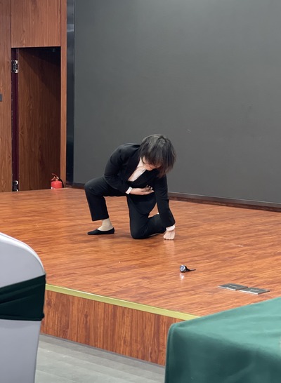 White shirt and black pants suit; left knee, sole of the right foot, and left hand on the floor
