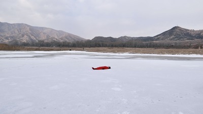 Low mountains in the distance; lying on the back on a completely frozen white lake surface