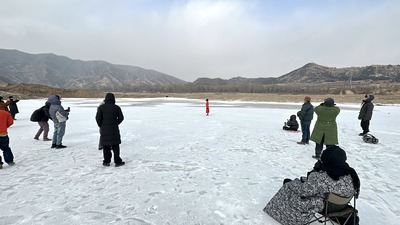 Audience members witnessing and watching on the same ice; in the distance, mountains and a red line